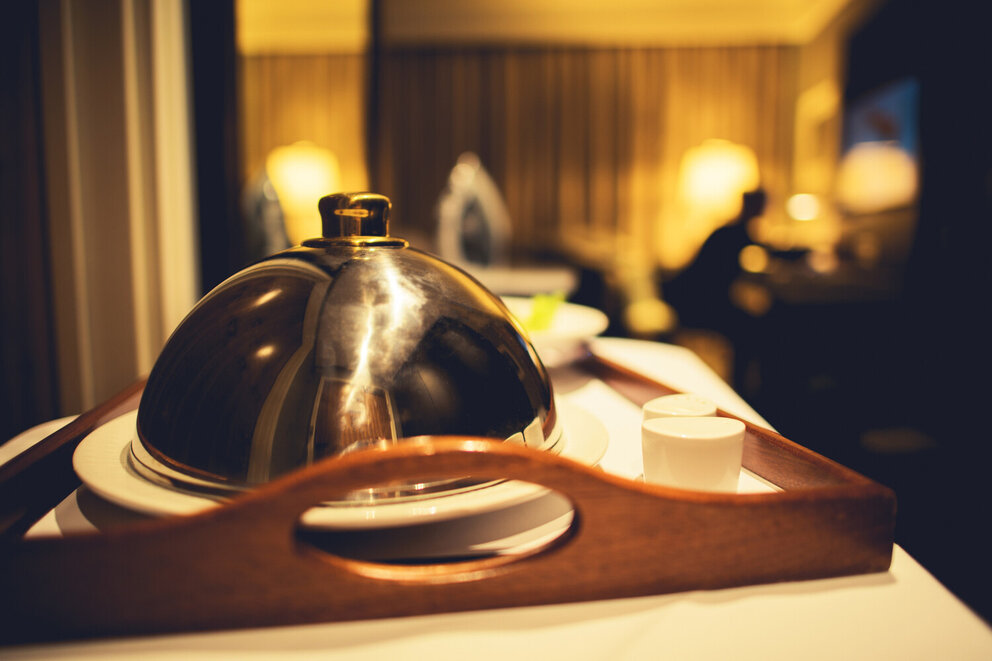 a silver serving dome on a plate sits on a wooden tray with a cup
