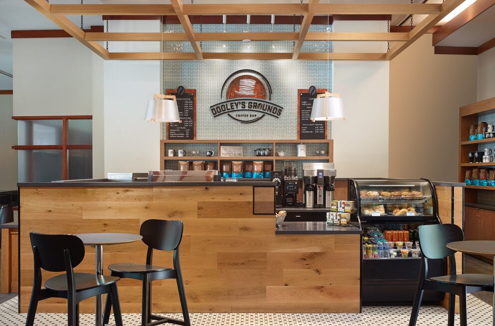 A modern coffee bar with a wooden counter, pastries, and seating area.
